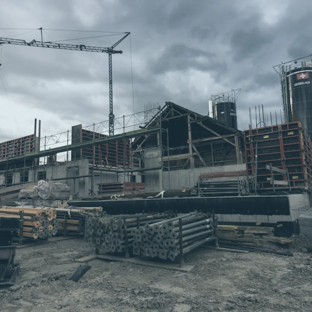 Tower crane above a building under construction, with scaffolding and stacked materials, with a subtle blue tint.