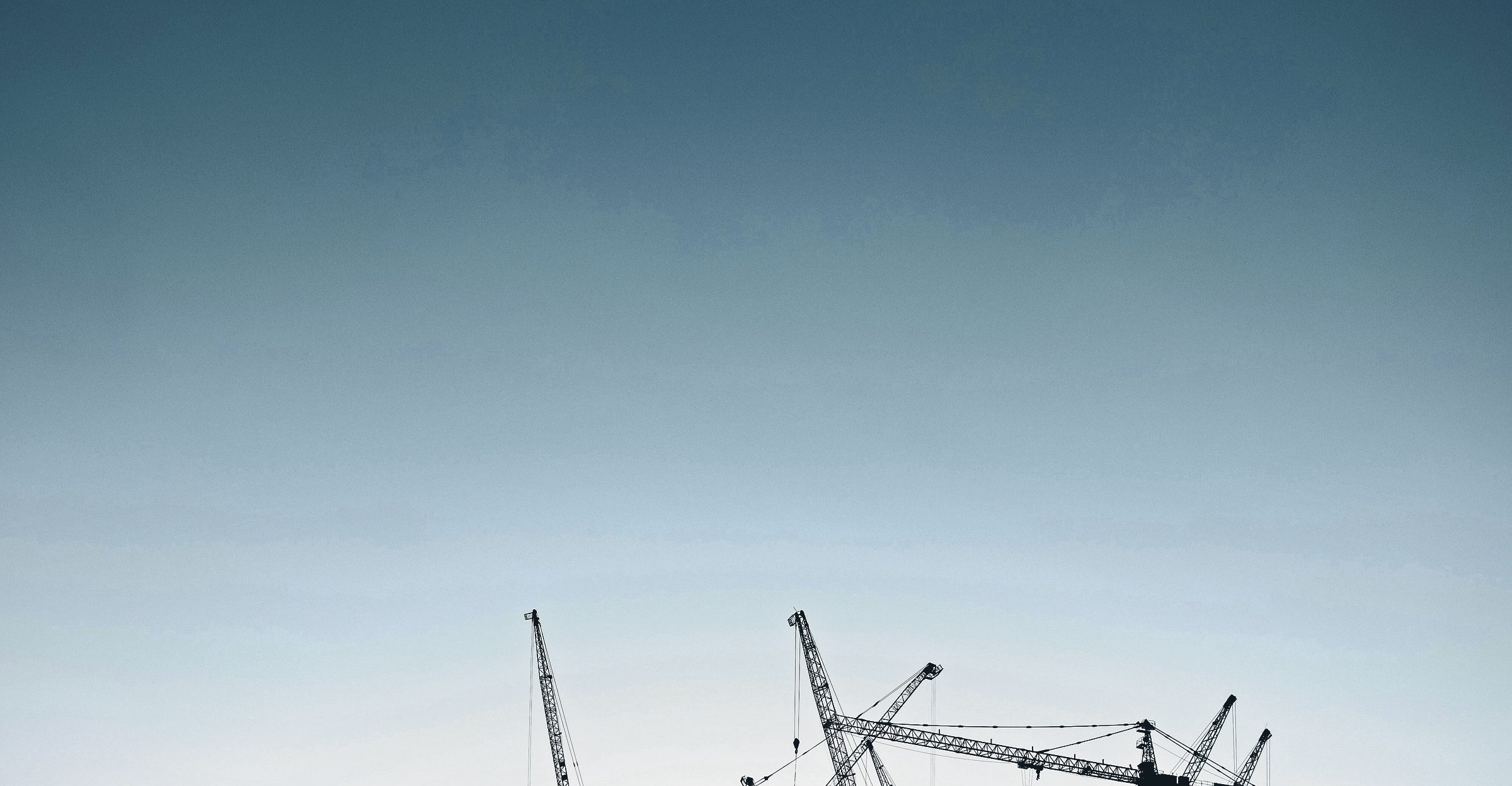 A wide, calm dusk sky with the tips of tower cranes rising into it from below.