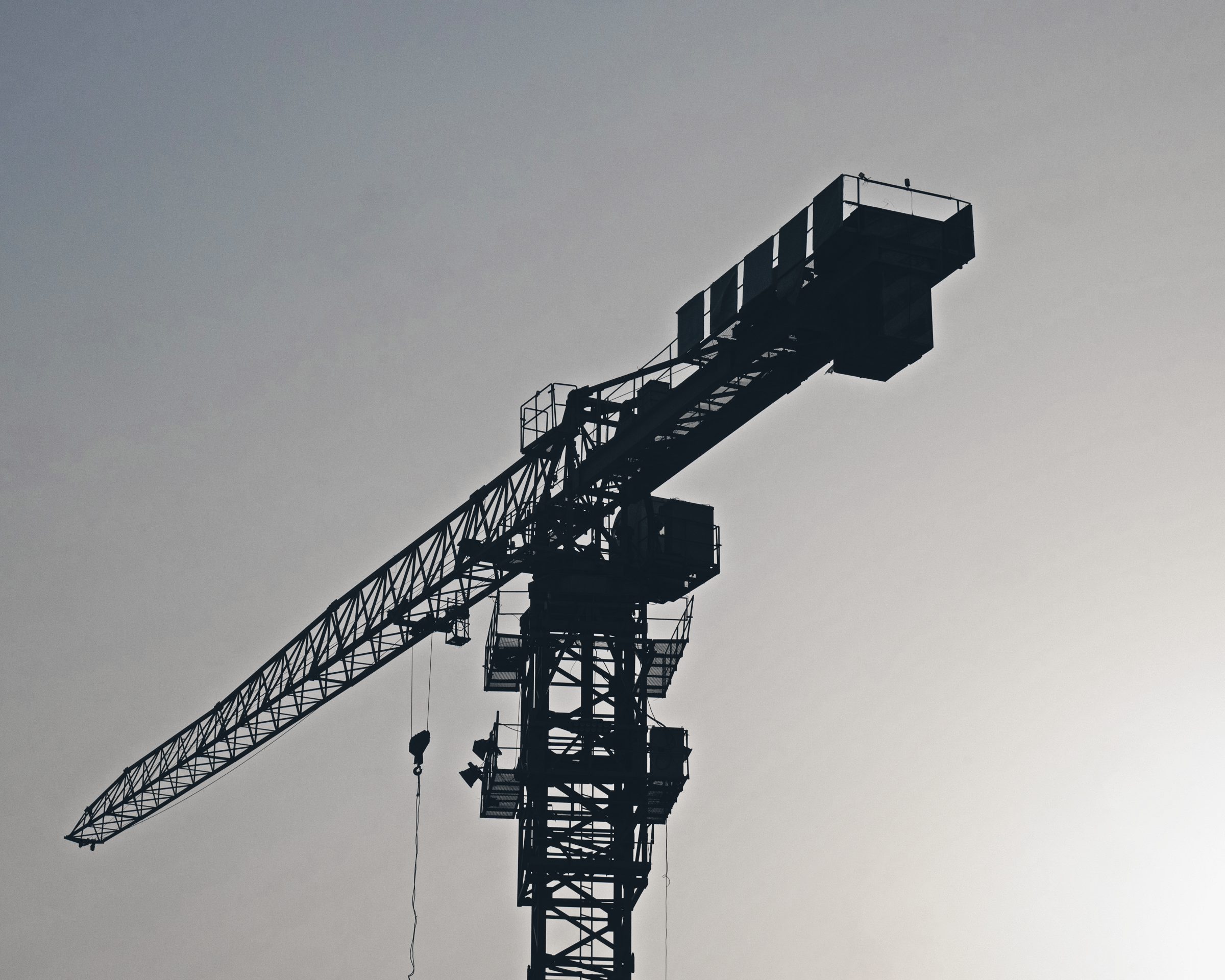 Silhouette of a tower crane against a smooth evening sky, most of the frame open sky.