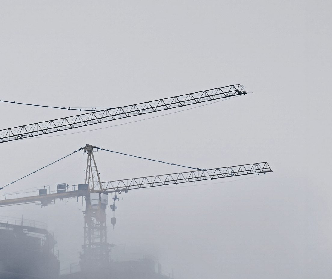 Two tower crane jibs dissolving into low winter cloud.