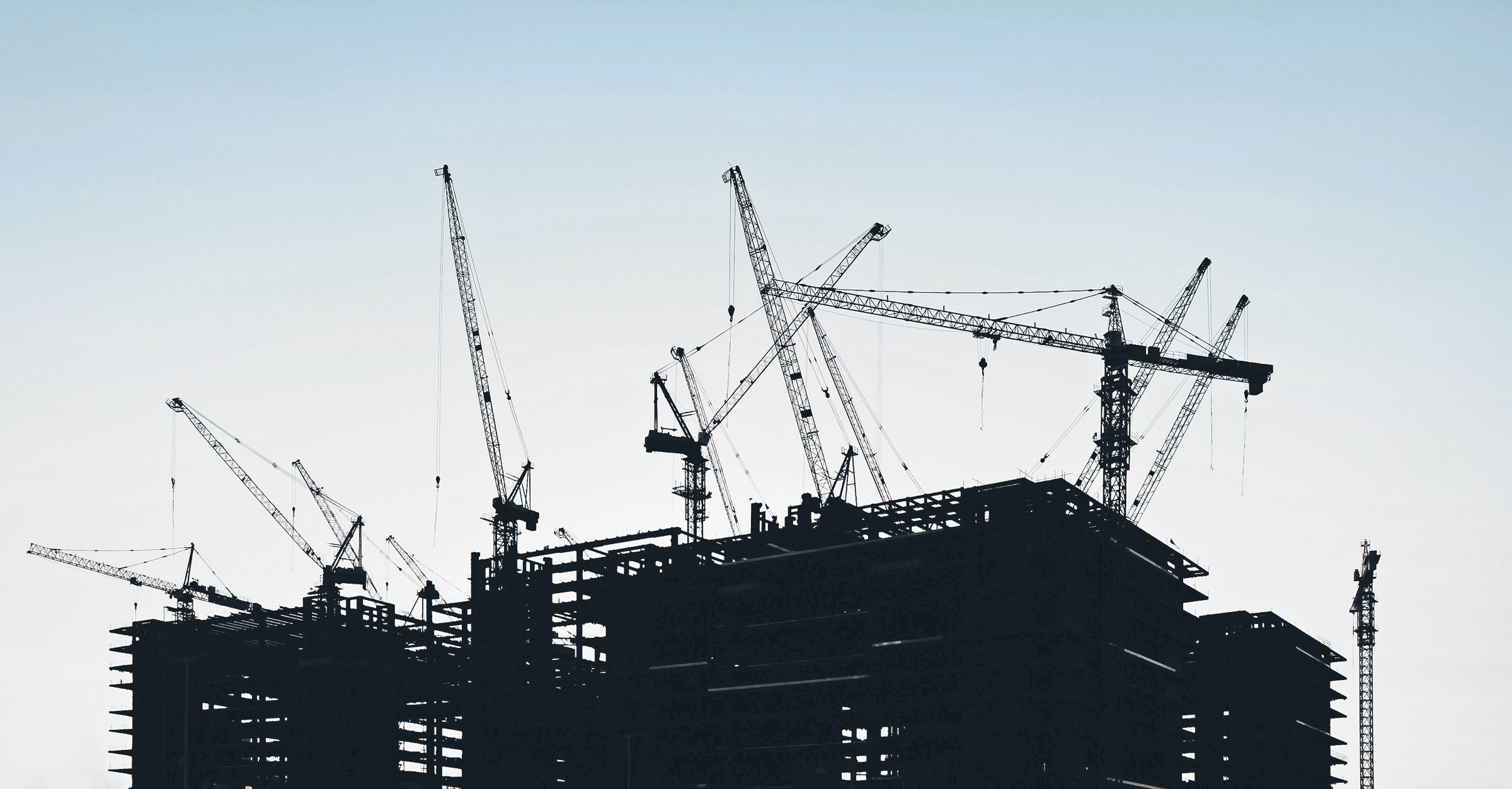 Silhouettes of a dozen tower cranes working over the frames of high-rise buildings at dusk.