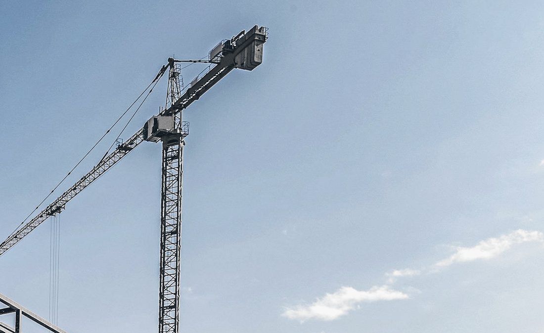 A yellow tower crane with its counter-jib and cab against a blue sky with a few clouds.