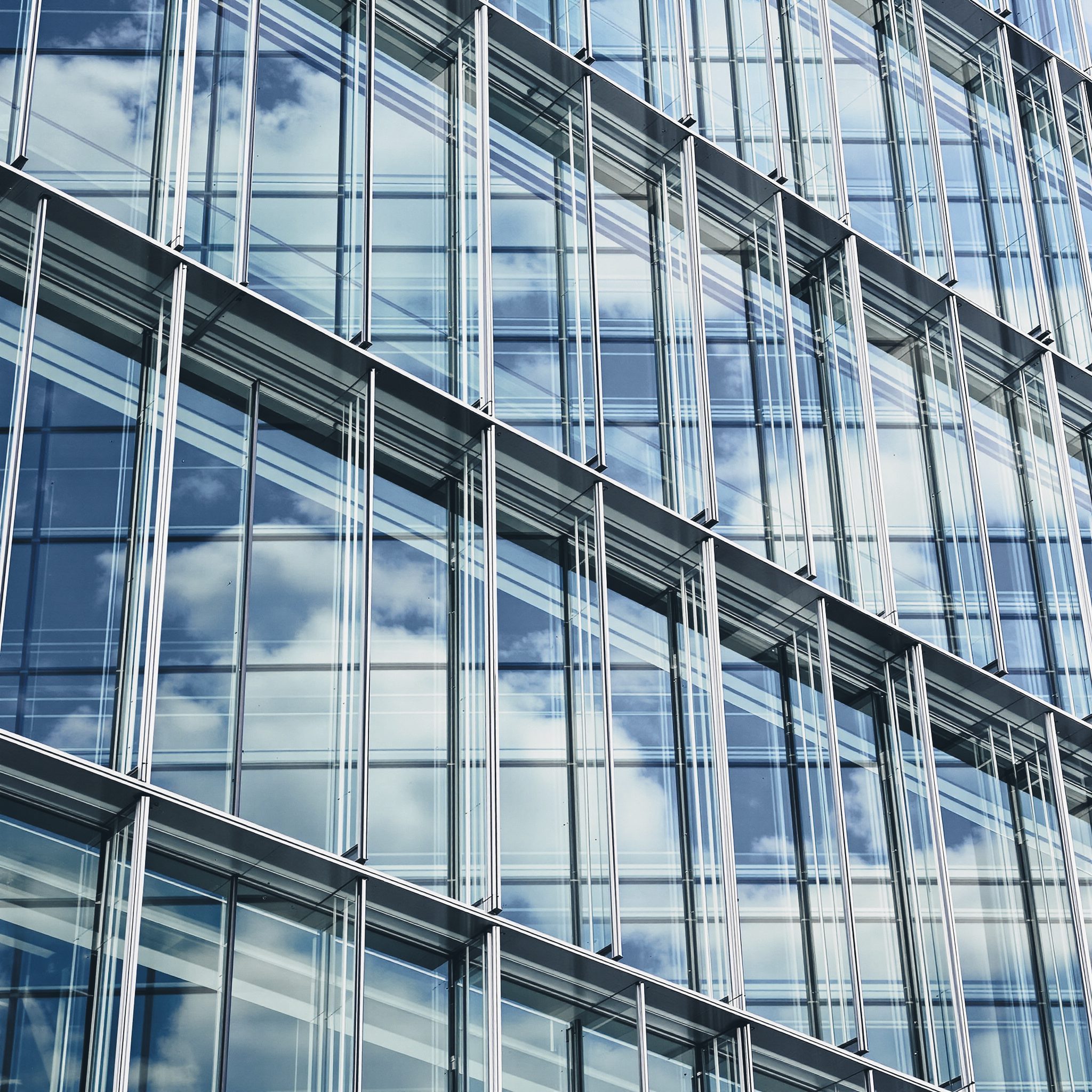 Close-up of a double-skin glass facade, glass fins and slab-edge bands reflecting clouds.