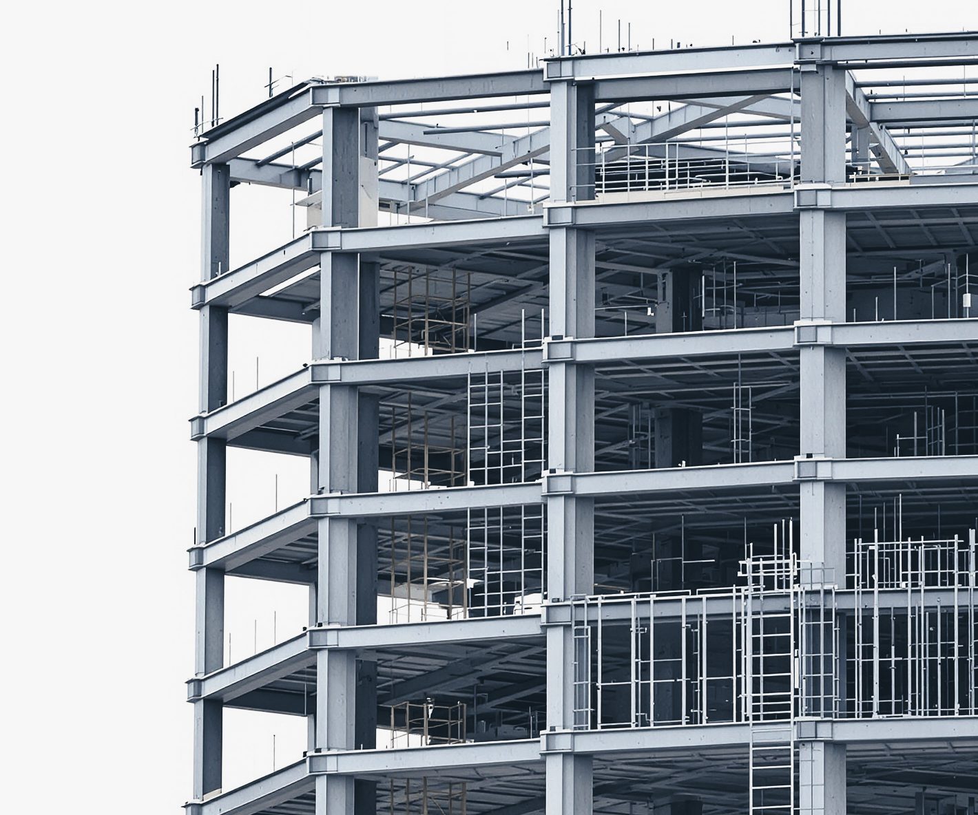 The top floors of a grey structural steel frame under construction, with metal deck and ladders, against a pale sky.