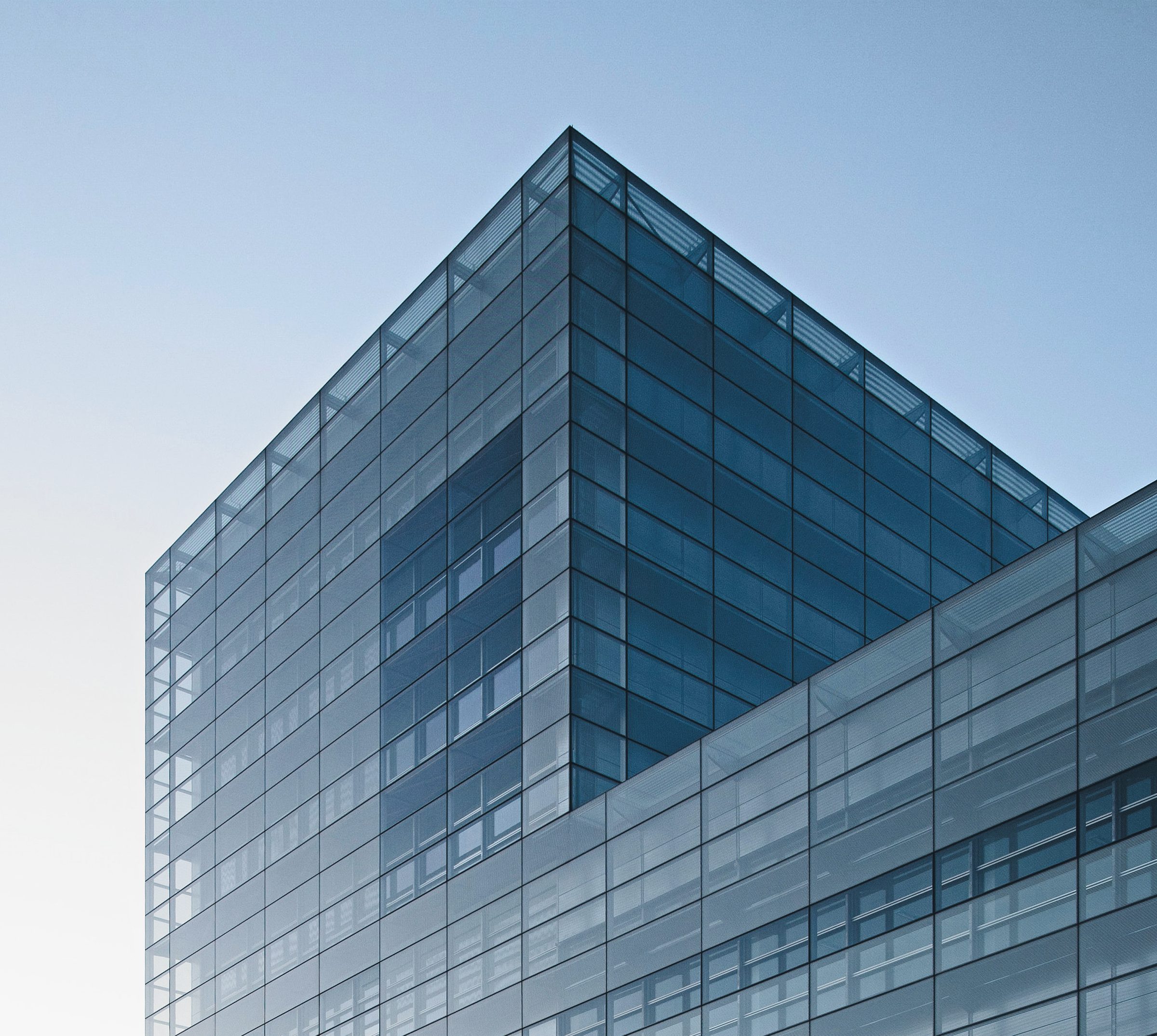 Low-angle view of a glass curtain-wall tower, its blue glazing grid rising against a clear sky.