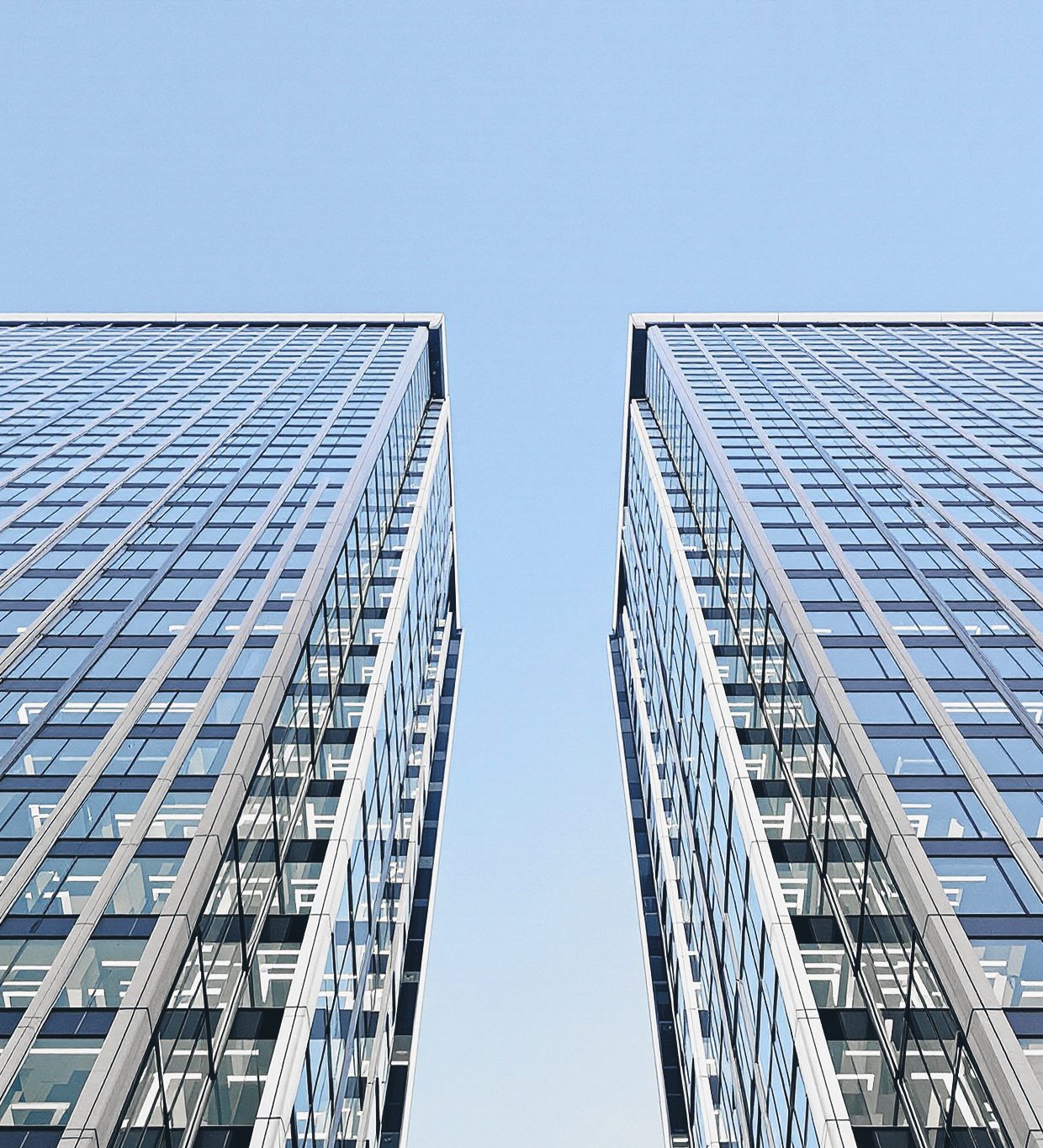 Looking straight up between two glass towers, with a band of clear blue sky between them.